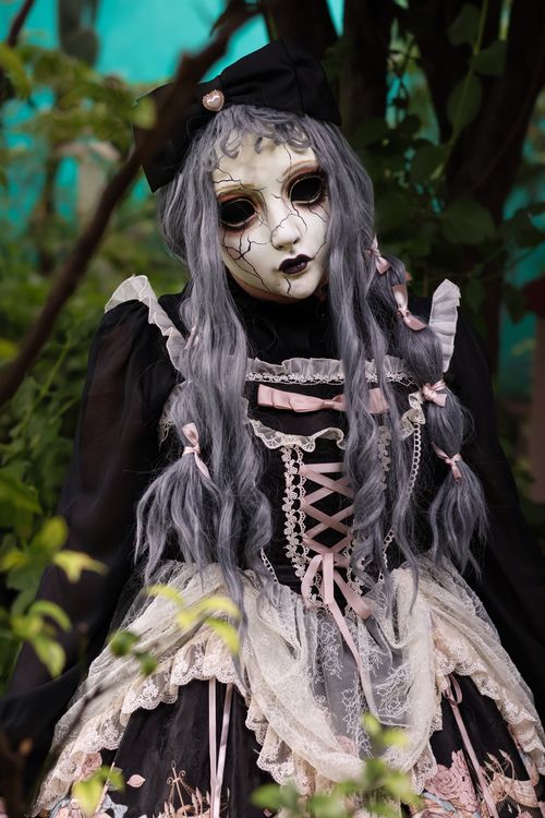 Free Creepy doll character in a dark, Victorian-inspired outfit surrounded by foliage. Stock Photo