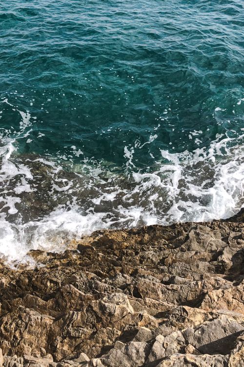 Free A mesmerizing view of waves crashing onto a rocky shore with vibrant blue ocean water. Stock Photo