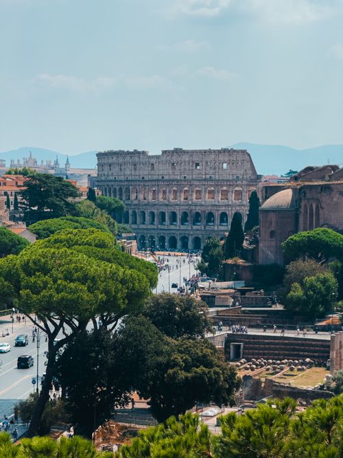 Free Aerial view of the historic Colosseum surrounded by lush greenery on a sunny day in Rome. Stock Photo
