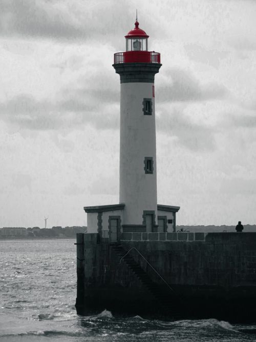 Free A picturesque lighthouse with a red top stands against a cloudy sky by the sea. Stock Photo