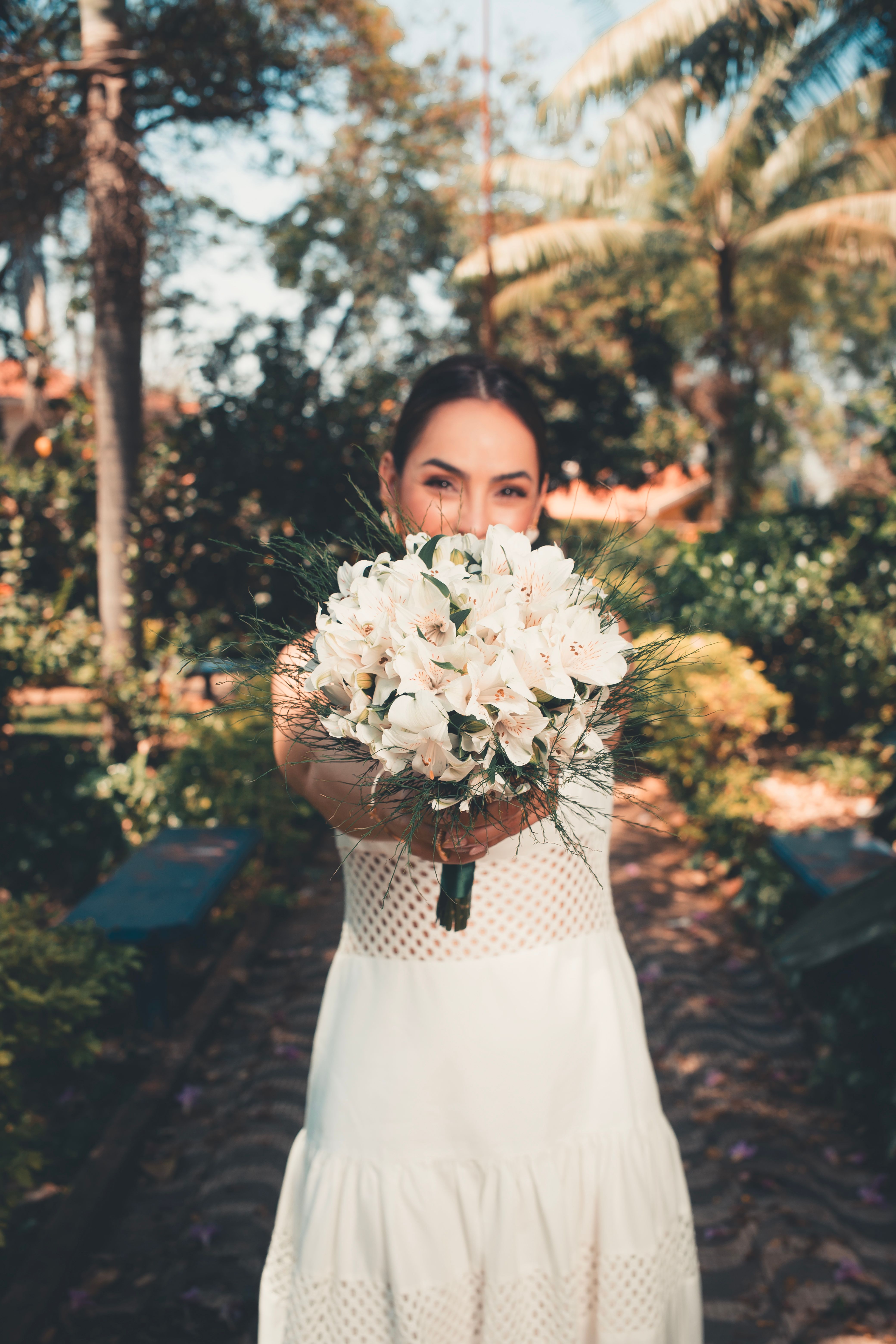 A bride joyfully holds a bouquet of white flowers in a sunny garden setting.