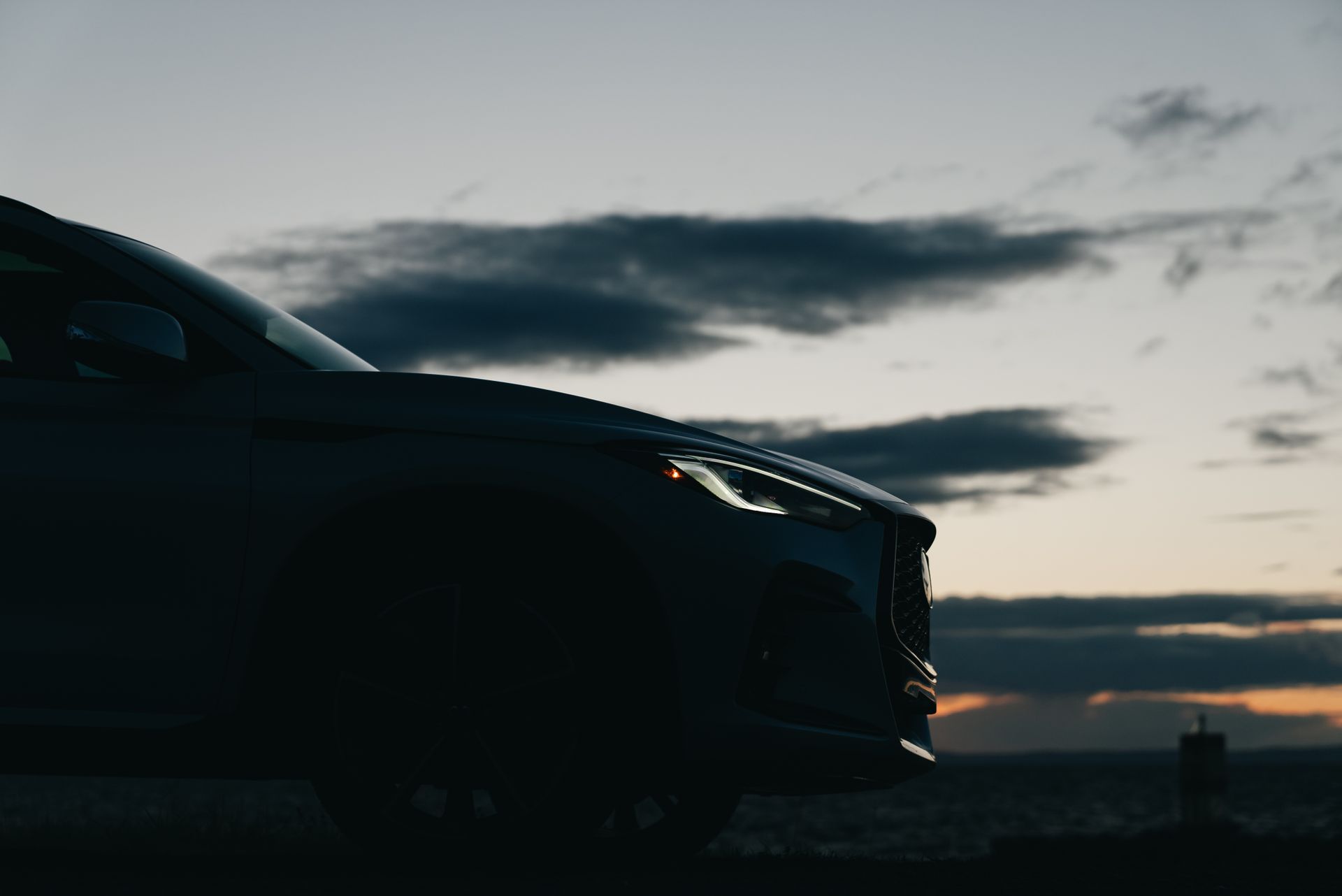 Side profile silhouette of a car against a dramatic sunset, highlighting its sleek design.