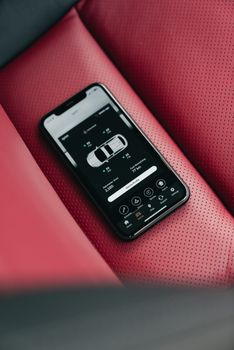 Smartphone showing car control app on red perforated leather car seat, close-up.