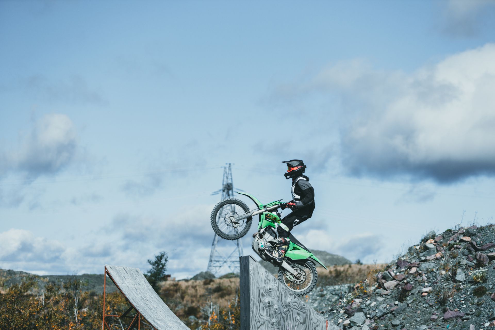 A motorcyclist performs an impressive jump over a ramp in a rugged outdoor setting.