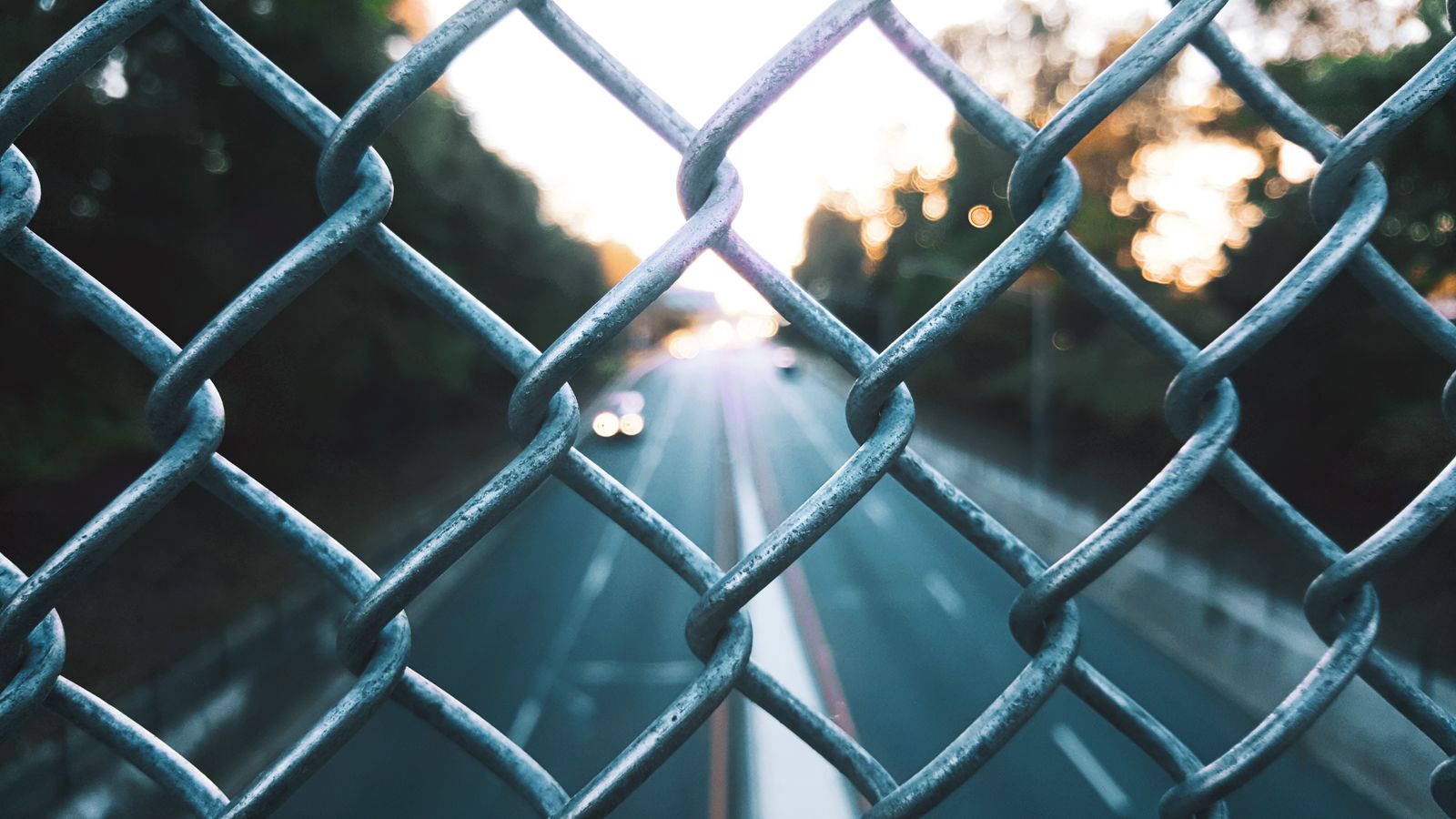 Chain-link fence in sharp focus with a blurred highway beyond at sunset