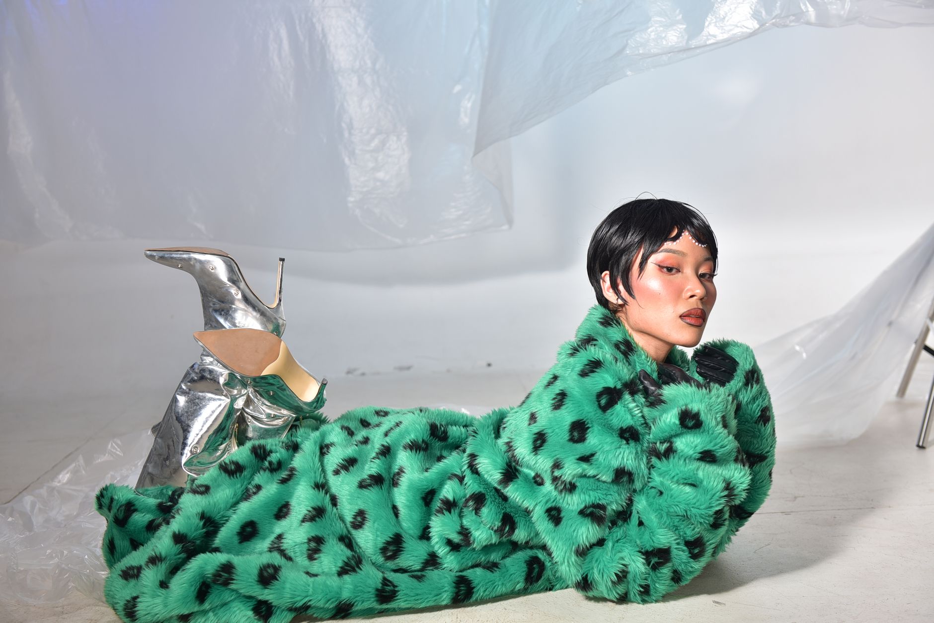 Stylish woman posing in a vibrant green fur coat and metallic silver boots indoors.