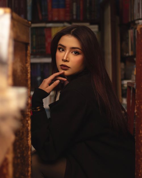 Free A thoughtful woman poses in a cozy library setting with warm, inviting light. Stock Photo