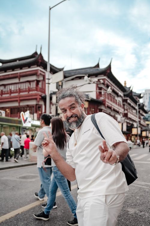 Free A happy man gestures cheerfully on a vibrant city street with traditional buildings in the background. Stock Photo
