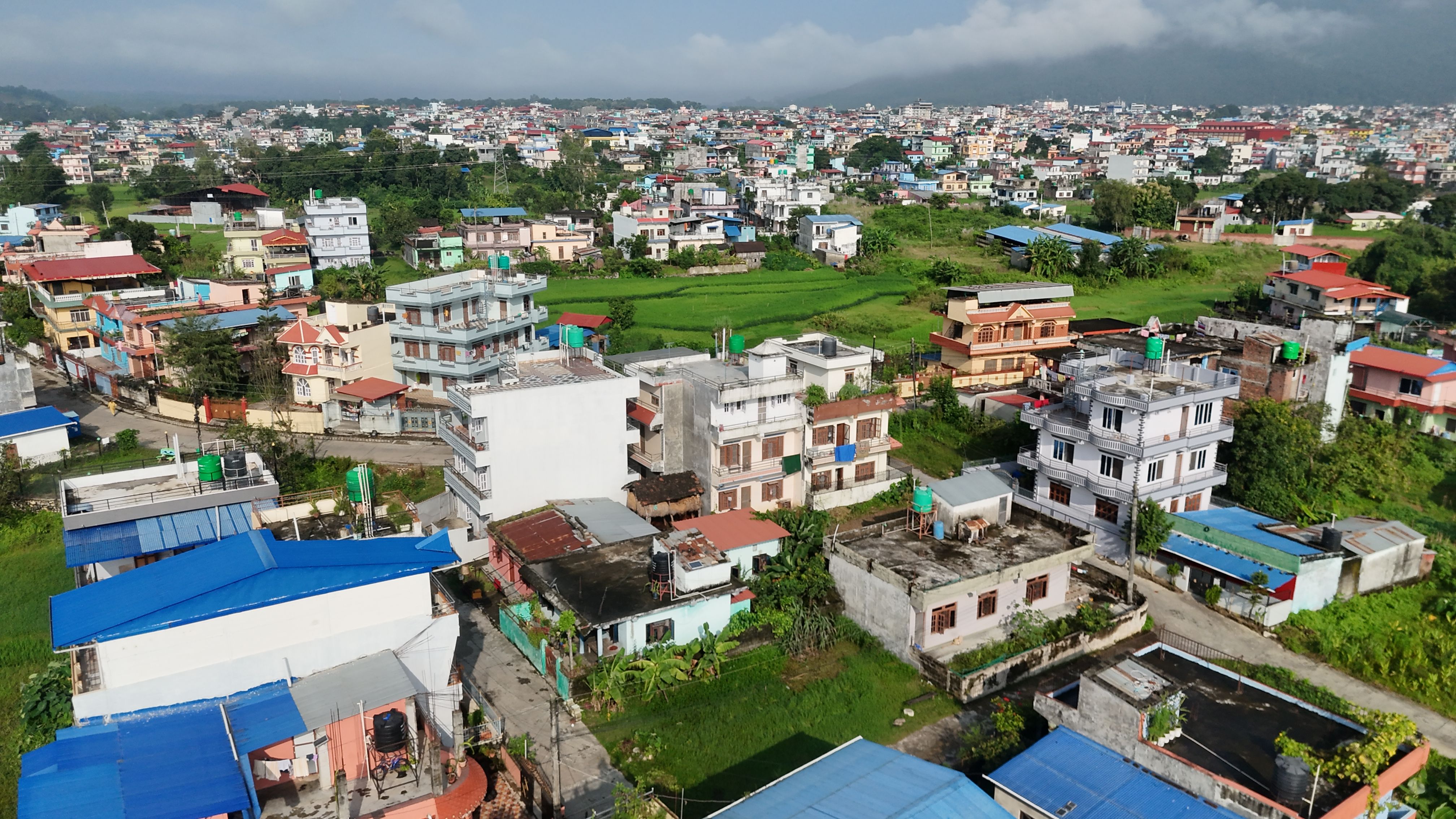 Outstanding Mount Everest Scenic Flight 50 Minutes Review: Is This Nepal Helicopter Tour Worth It? Review 2026 - Drone capture of a vibrant residential area with green fields in Nepal, showcasing colorful rooftops and mountainous background.