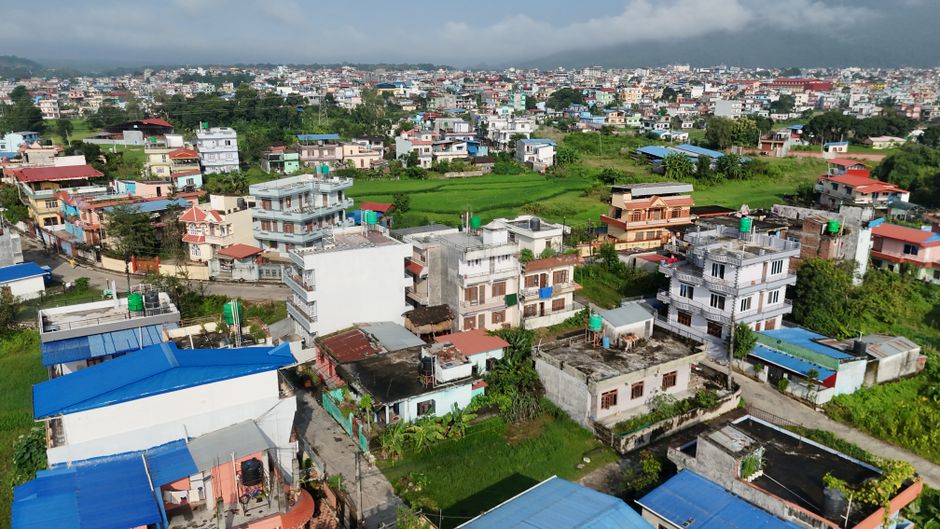 Outstanding Mount Everest Scenic Flight 50 Minutes Review: Is This Nepal Helicopter Tour Worth It? Review 2026 - Drone capture of a vibrant residential area with green fields in Nepal, showcasing colorful rooftops and mountainous background.