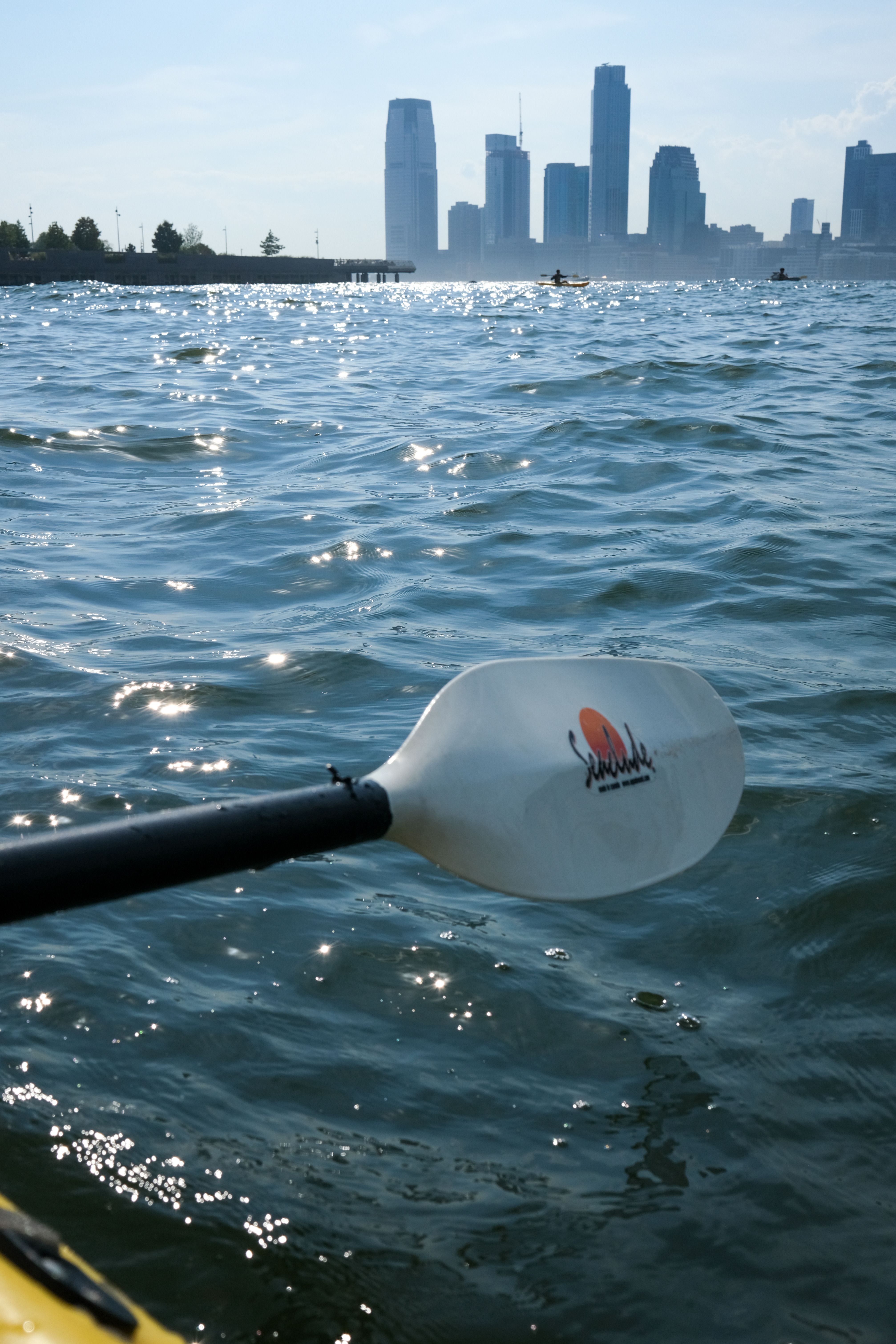 Kayak paddle on water with distant city skyline in bright daylight.