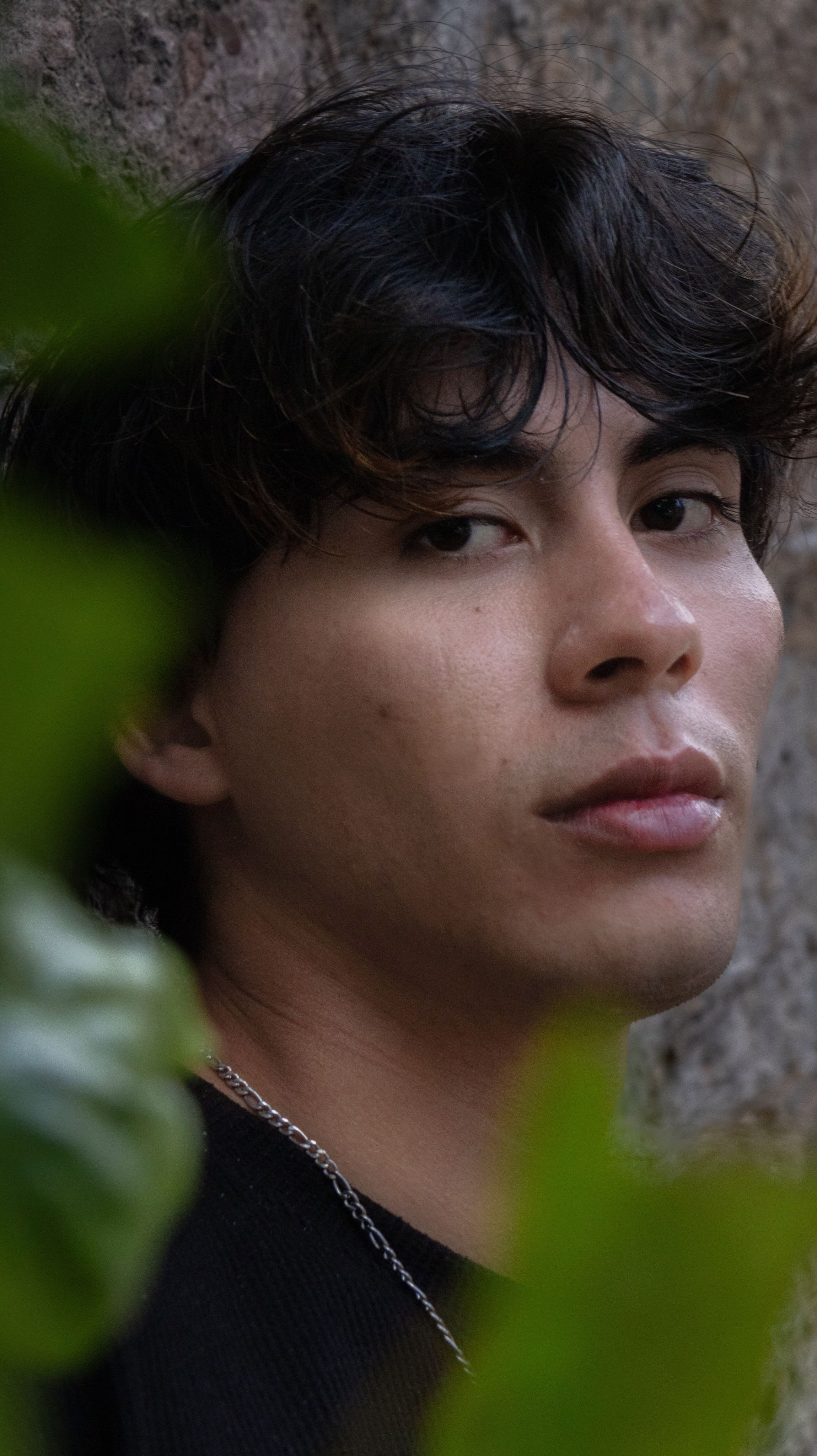 Thoughtful young man surrounded by urban greenery, exuding introspection and style.