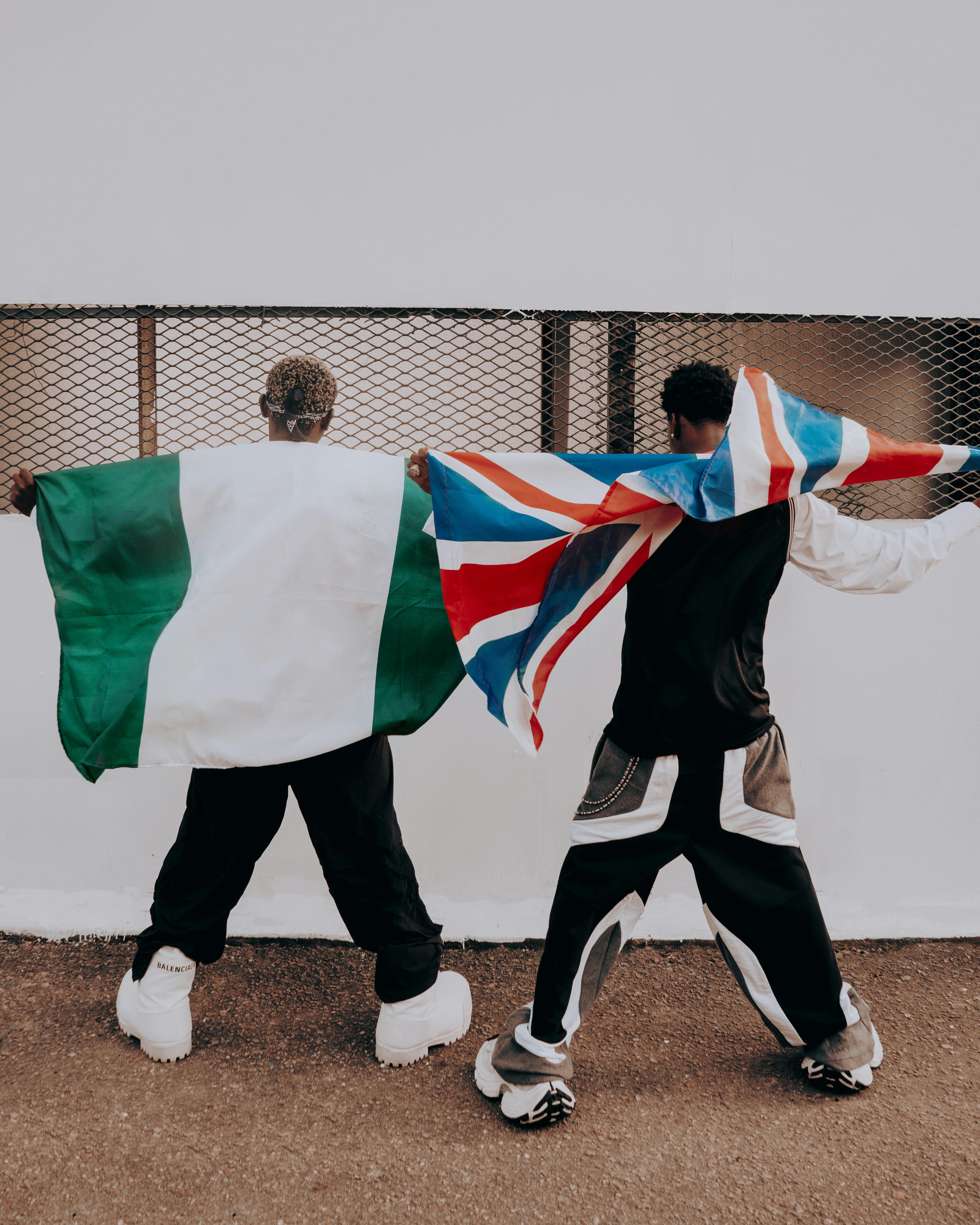 Two adults showing cultural pride with Nigerian and UK flags outdoors.