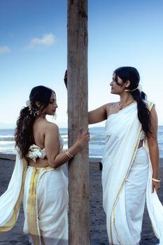 Two women in traditional Indian attire pose elegantly by the beach in Vancouver, highlighting cultural grace.