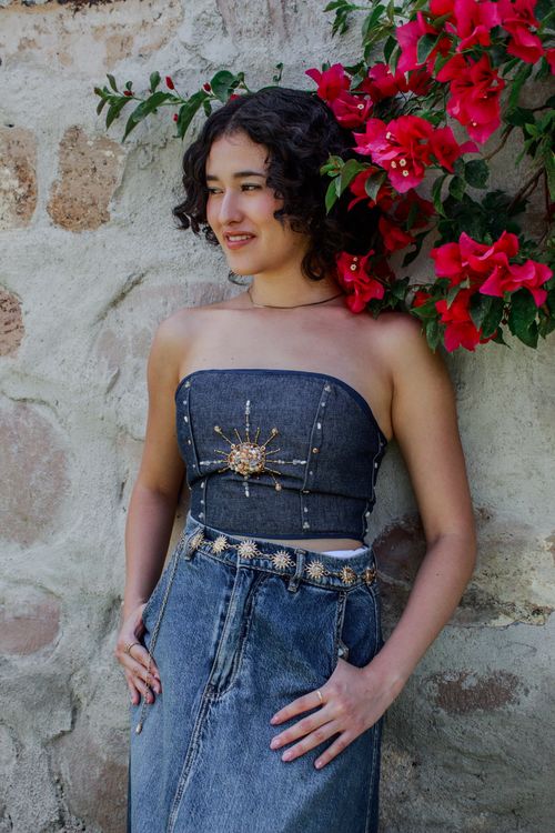 Free A woman poses elegantly in denim against a stone wall adorned with red flowers in Querétaro, Mexico. Stock Photo