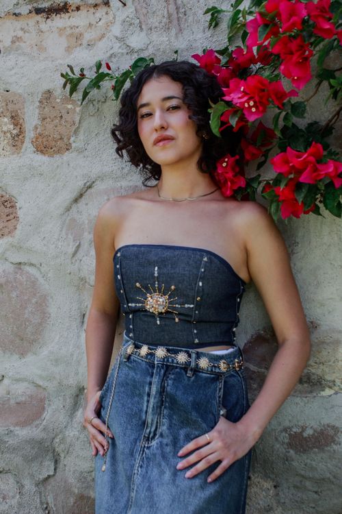 Free Stylish Mexican woman posing against stone wall with vibrant flowers in Querétaro, Mexico. Stock Photo