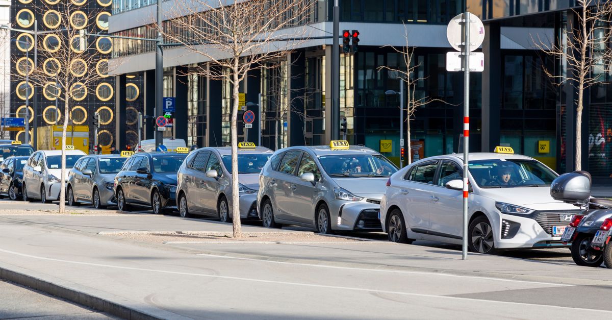 A white Cruise autonomous taxi with roof-mounted sensors drives along a paved city road in bright daylight.