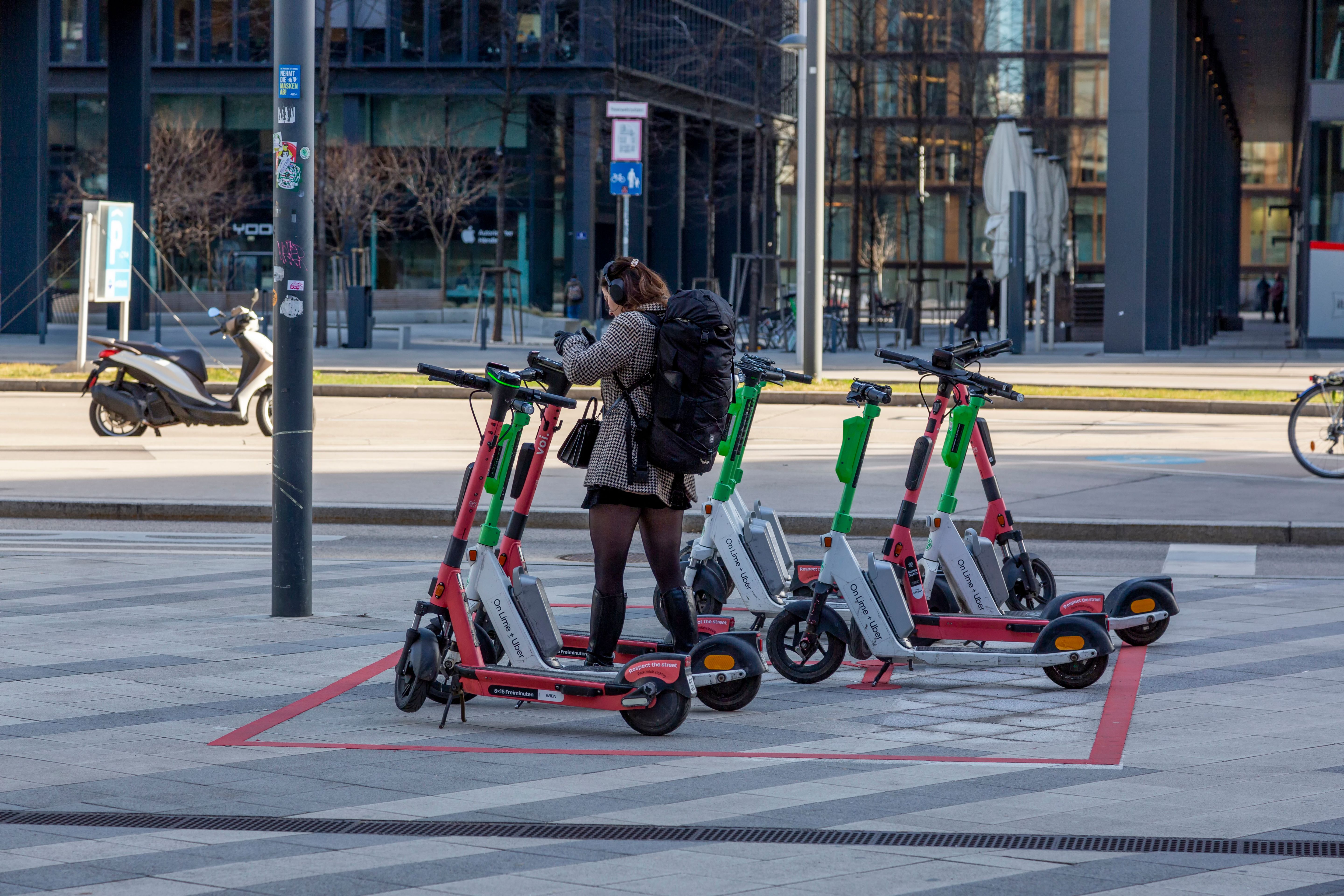 A young adult uses rental scooters at an urban parking spot.