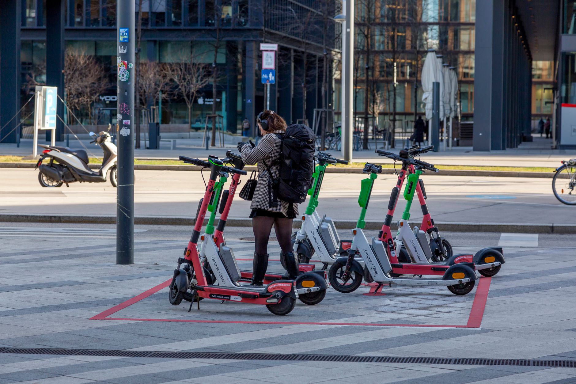 A young adult uses rental scooters at an urban parking spot.