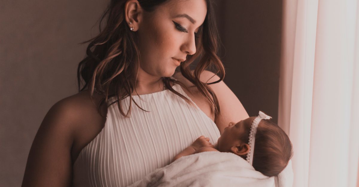 A mother lovingly cradles her baby by a window, capturing a tender moment.