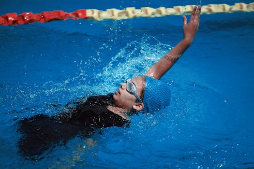 A teenager in a swimming pool doing backstroke, wearing a blue cap.