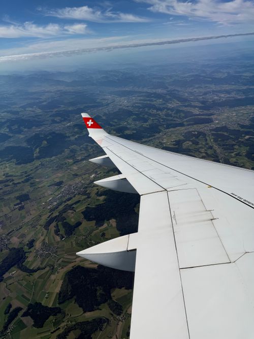 Free Airplane wing flying over scenic Swiss landscape with clear sky and mountains. Stock Photo