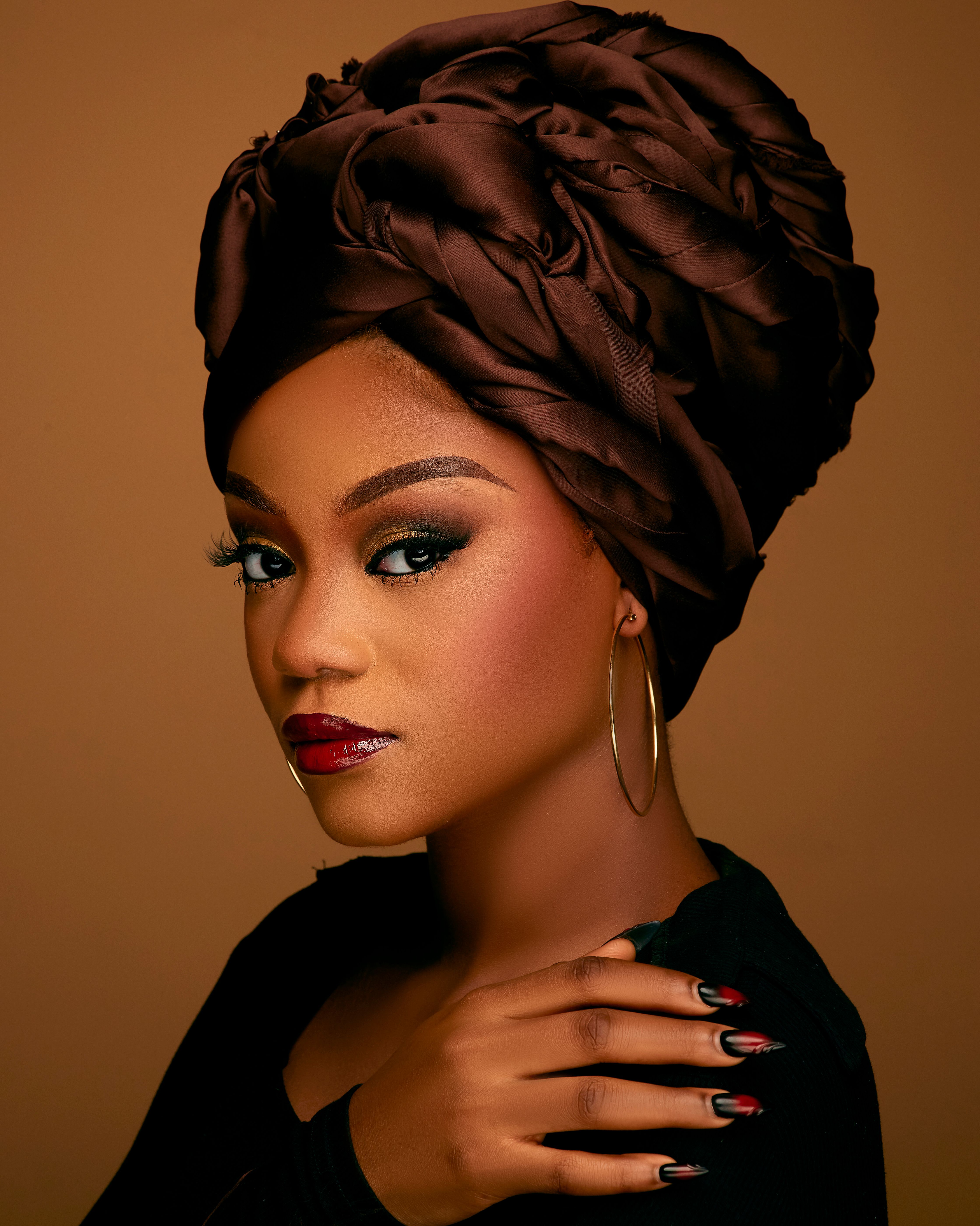 Stylish portrait of a woman wearing a brown headwrap with bold makeup.
