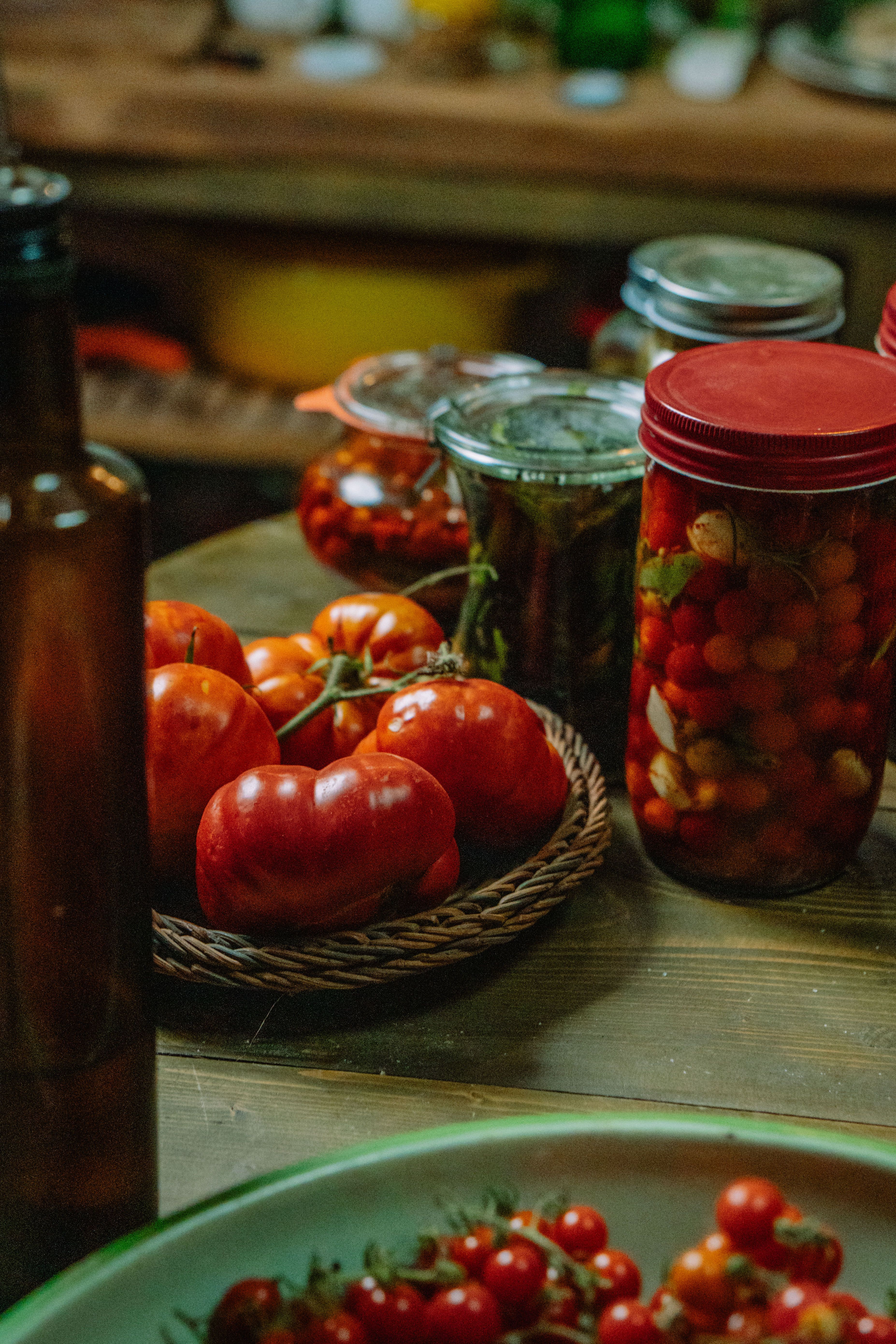 Fresh tomatoes and jars of preserved vegetables on a rustic kitchen table