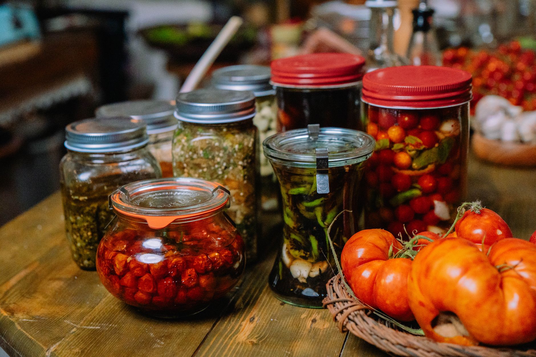Vidros de conserva caseira de tomate e figos em calda alinhados numa bancada de cozinha rústica