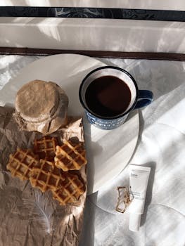 Warm morning setup with coffee, waffles, and a jar on a bright table.