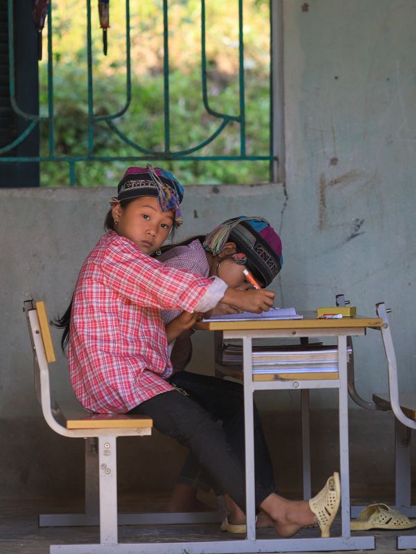 Two children in warm clothing studying at a desk in a rural Vietnamese classroom