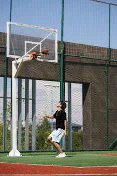 A teenager in sports attire playing basketball at an outdoor court during the day.