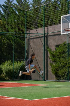 Energetic young man performing a jump shot on an outdoor basketball court.