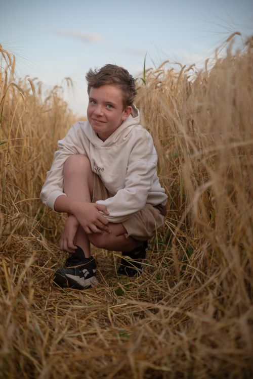Free A cheerful boy crouching in a golden wheat field during sunset, showcasing nature's beauty. Stock Photo