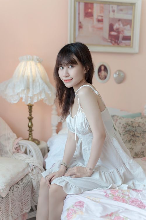 Free A woman in a white dress sits on a cozy bed in a beautifully decorated bedroom. Stock Photo
