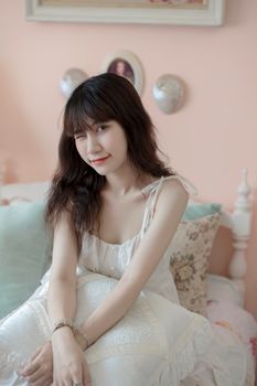 A young woman in a white dress sits comfortably in a soft, pastel-themed bedroom.