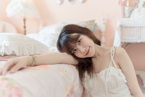 Free A young woman relaxes in a softly lit bedroom with pastel decor and gentle ambiance. Stock Photo