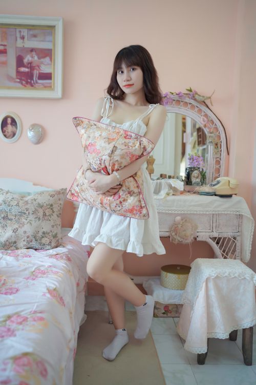 Free Adult woman holding floral pillow in vintage-style bedroom, creating a soft and cozy atmosphere. Stock Photo