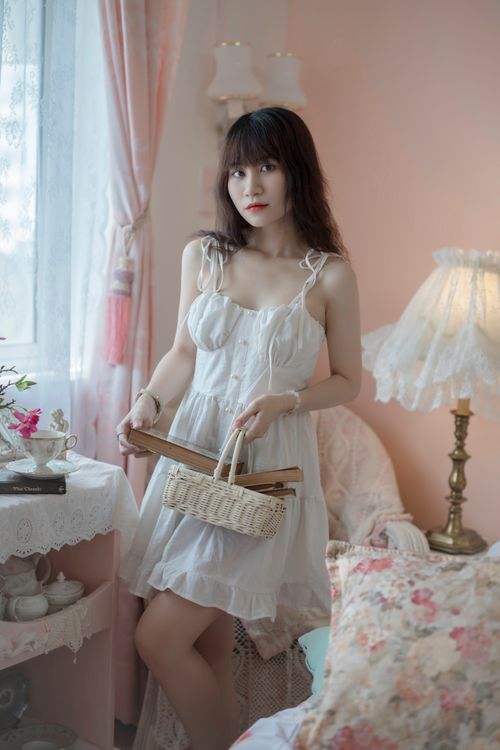 Free A young woman in a white dress holding a basket in a softly lit vintage-styled room. Stock Photo