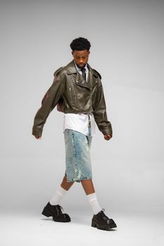 A young man showcases trendy fashion with a leather jacket and denim shorts in a stylish pose.