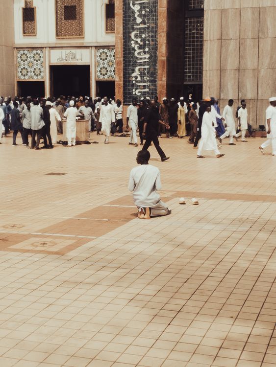 Man Praying Outside a Busy Mosque Courtyard · Free Stock Photo