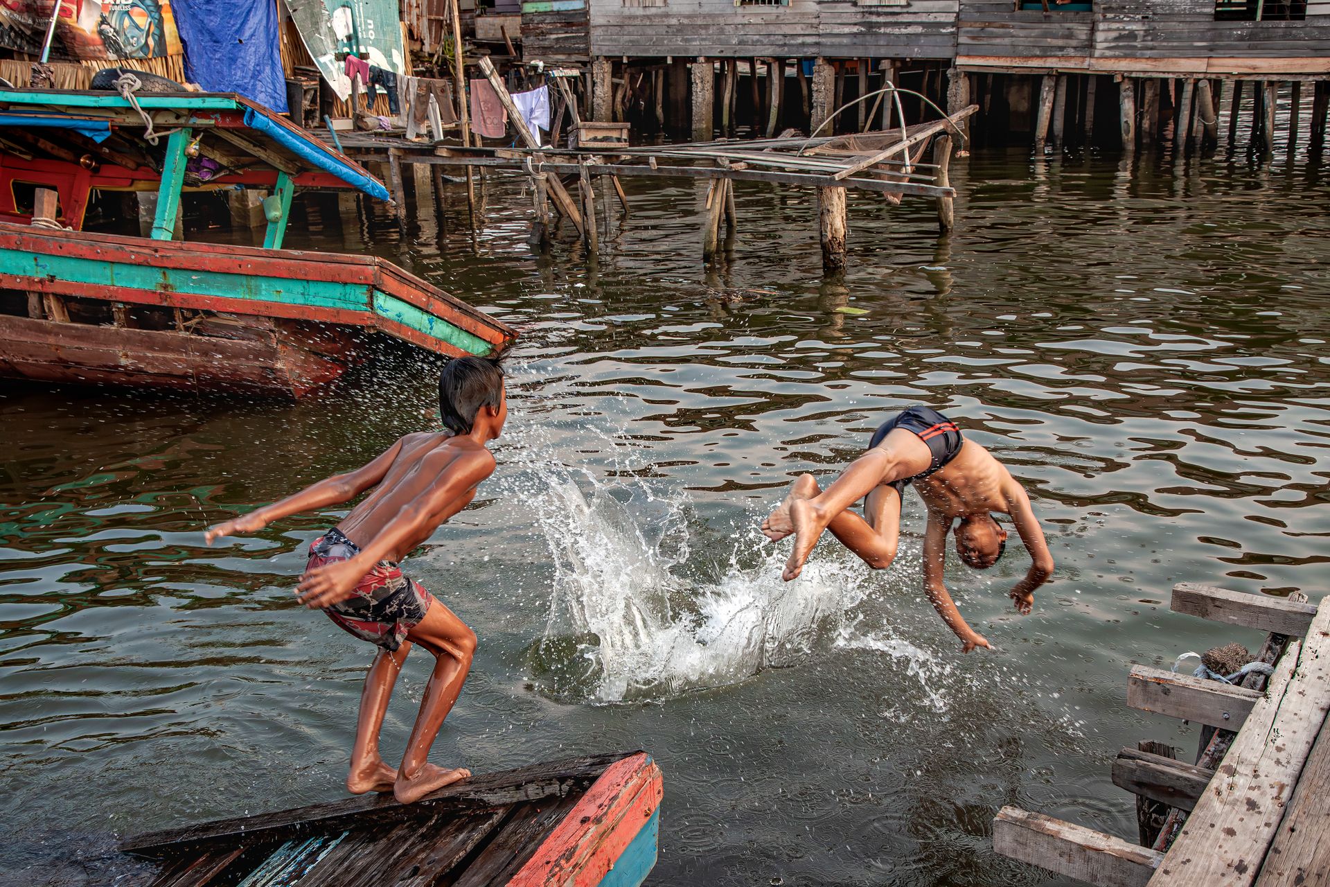 Two boys joyfully dive into water from a wooden dock, capturing a sense of summer fun and adventure.