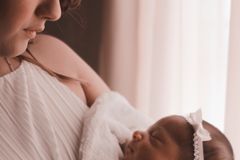 Tender moment of a mother holding her newborn child by a window, capturing love and warmth.