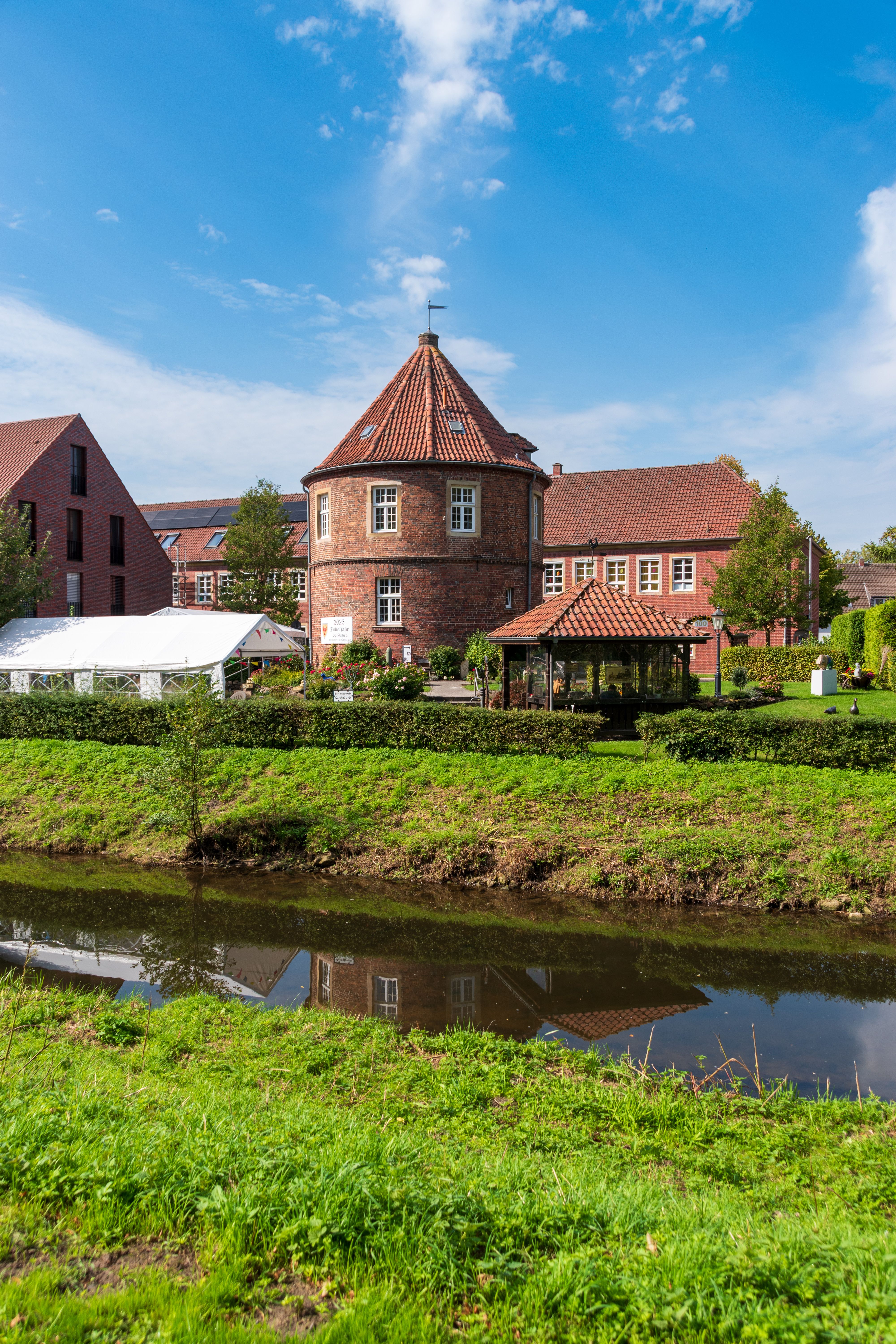 Charming historic brick building by a serene stream under a bright blue sky. Ideal for architecture and travel themes.
