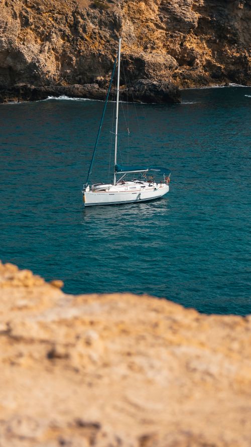 Free A serene sailboat floats on deep blue waters near rugged coastal cliffs. Stock Photo