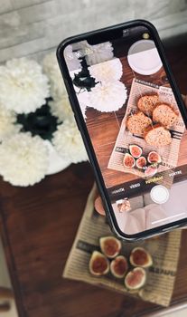 Flat lay capturing figs and muffins with a floral background using a smartphone.