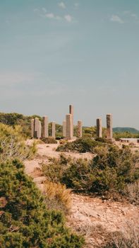 Desert view of historical stone pillars surrounded by nature under bright daylight.
