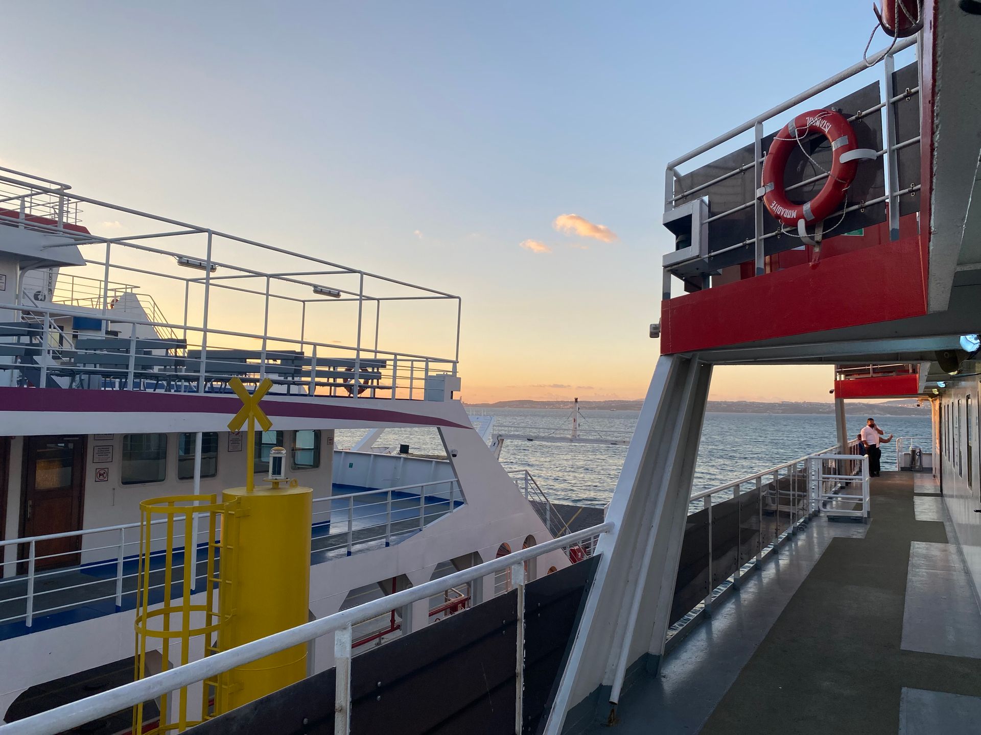 Calm sunset scene from a ferry deck with ocean view and safety equipment.