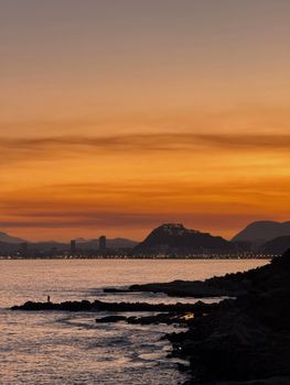 Dramatic sunset with silhouette of Alicante's skyline and coastline, offering a serene mood.