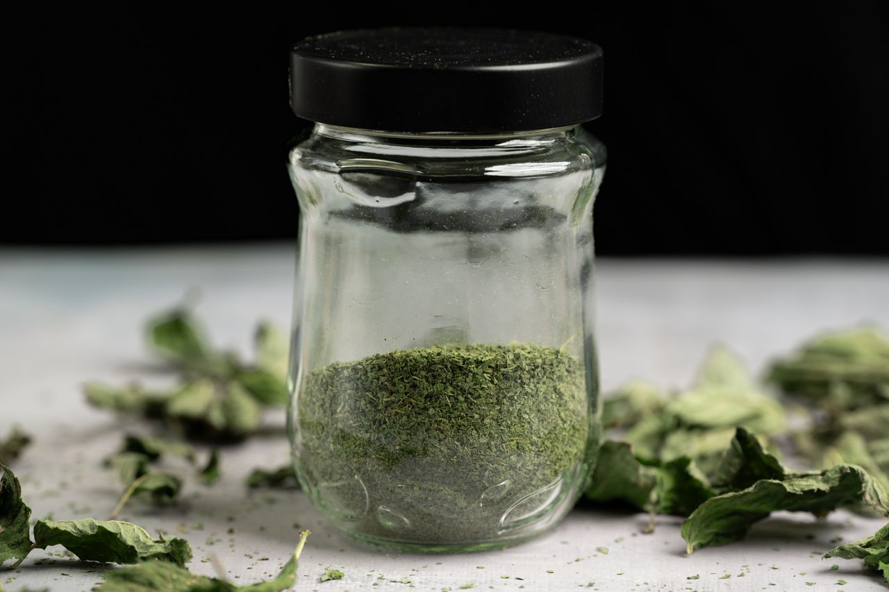 Small glass jar of ground dried mint with dried leaves scattered beside it